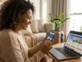 Viajante analisando pacote de viagem promocional no celular com passagem aérea, hotel e mala sobre a mesa