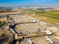Vista aérea do Aeroporto Internacional de Guarulhos com terminais, pistas e aviões estacionados em um dia ensolarado.