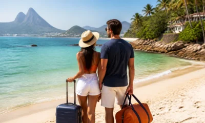 Lugares baratos para viajar em fevereiro: como fugir do Carnaval - Casal com malas observando uma praia brasileira em fevereiro