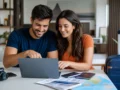 Preço do pacote de viagem é por pessoa ou por quarto? Saiba calcular - Casal analisando o preço de um pacote de viagem em um notebook